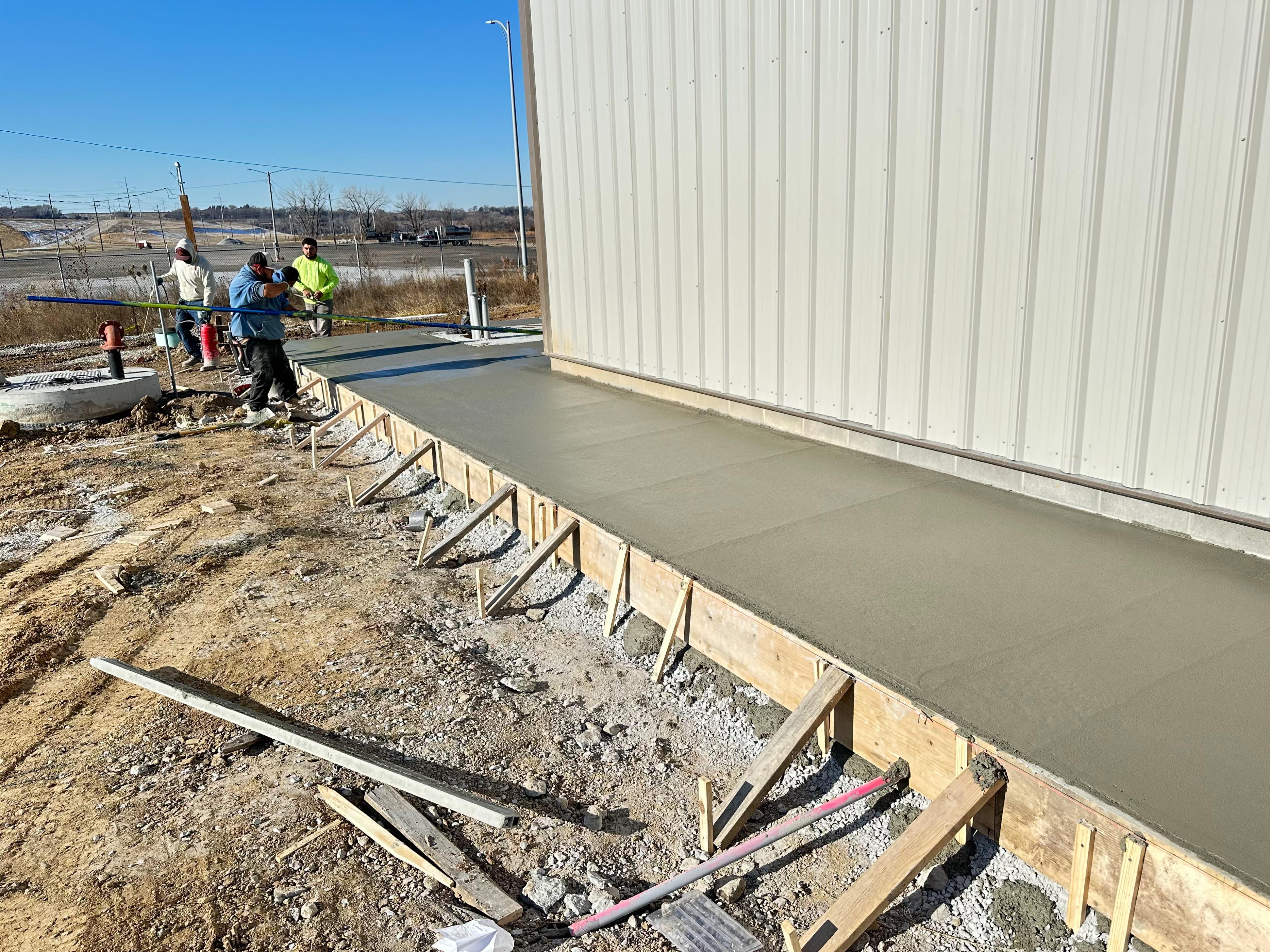 Commercial concrete sidewalk installation at metal-sided building by New Heights Contracting