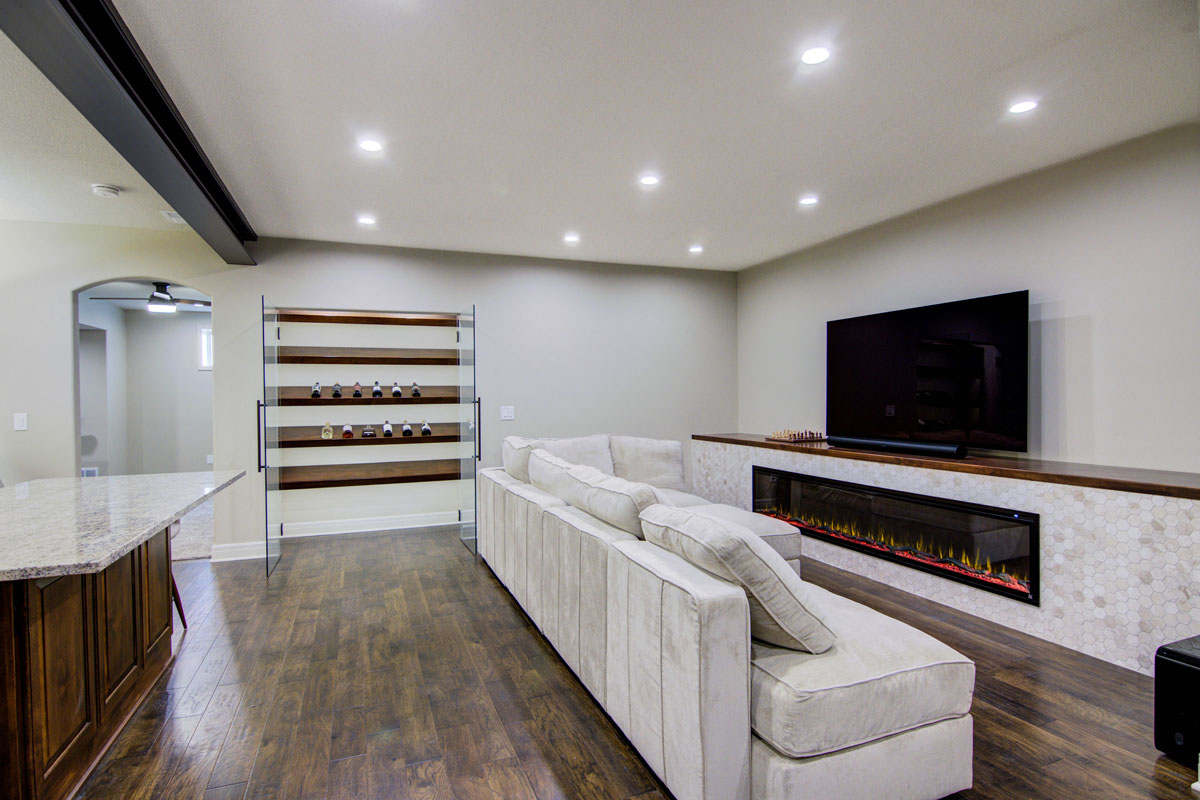 Finished basement in Omaha with modern entertainment area, electric fireplace, sectional sofa, and wet bar by New Heights Contracting