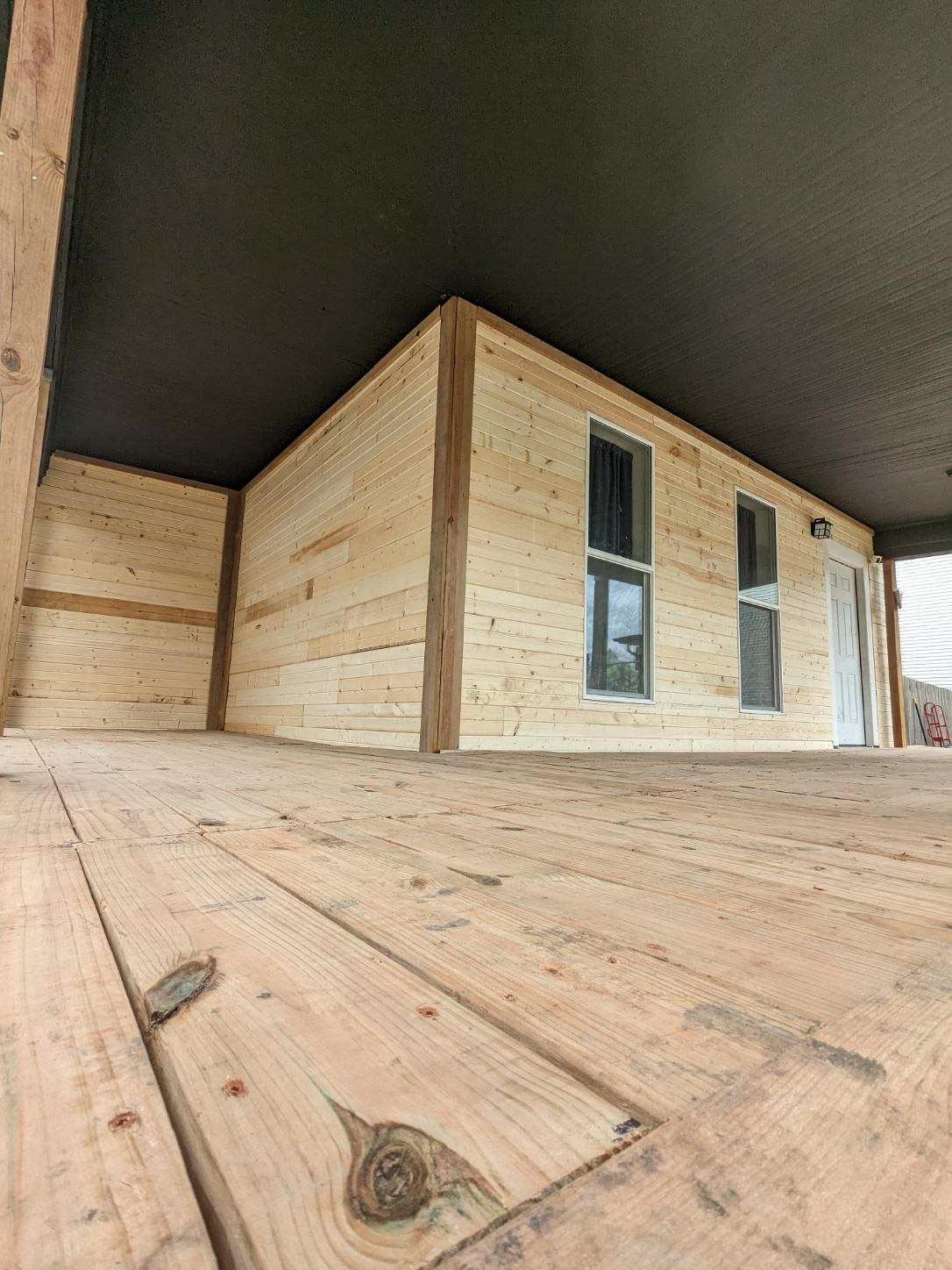 Custom covered porch with natural wood plank siding and deck flooring crafted by New Heights Contracting